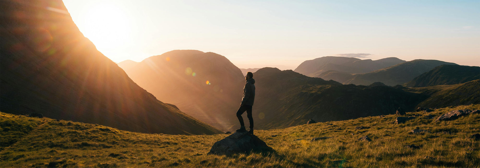 Person standing on a rock with mountains and sunset in the background
