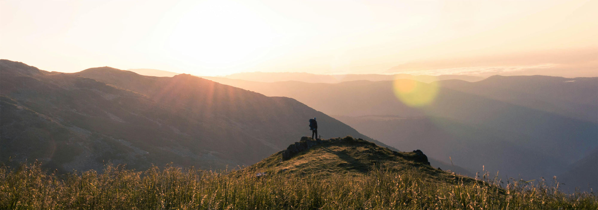 Person standing on a mountain top with the sun setting over the horizon