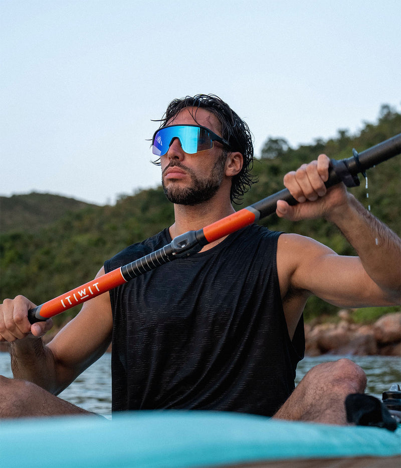 Man paddling a kayak with sunglasses on, surrounded by nature.