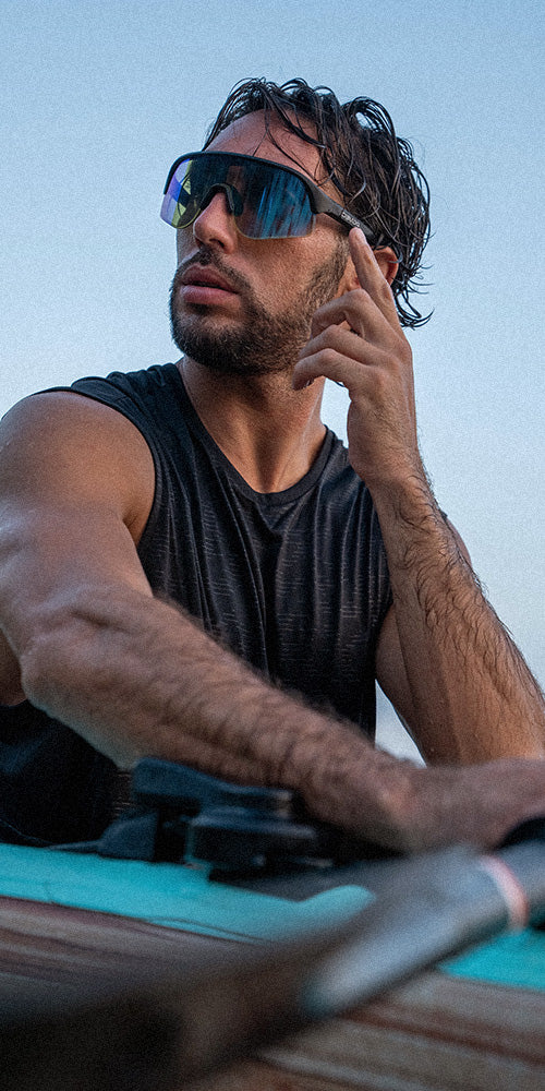Man wearing sunglasses and a black tank top, sitting on a boat with a blue sky background