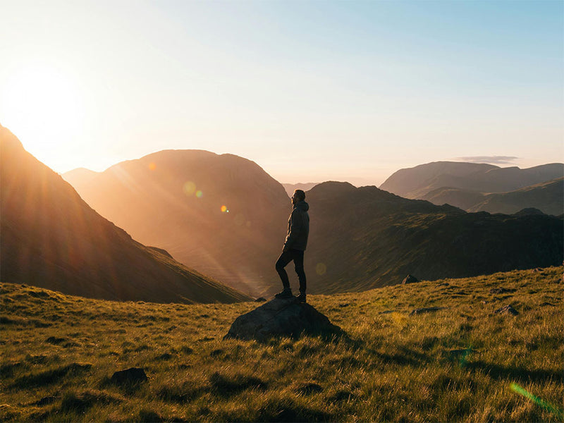 Person standing on a rock with mountains in the background during sunset.