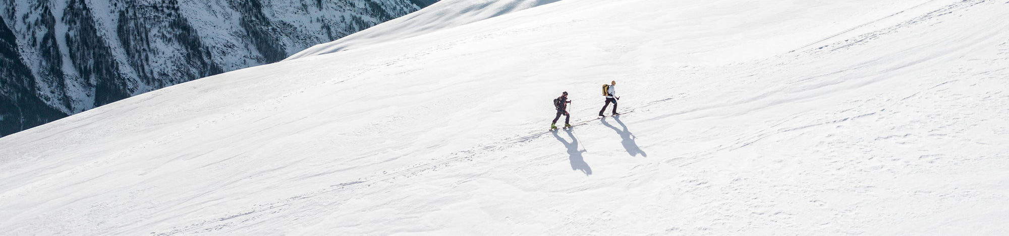 Two skiers on a snowy mountain slope with a clear sky above.