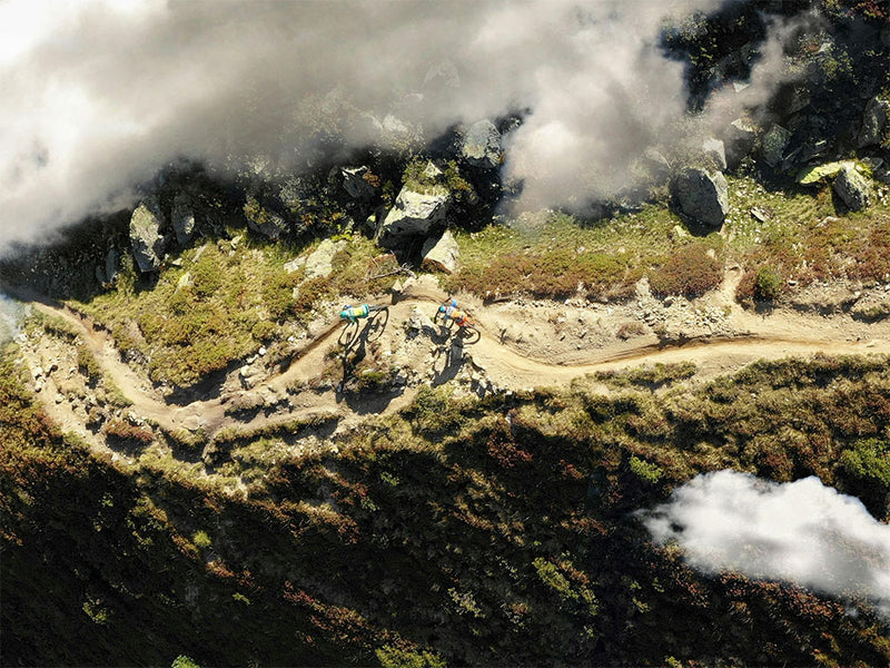 Two mountain bikers on a trail surrounded by mist and rocky terrain.