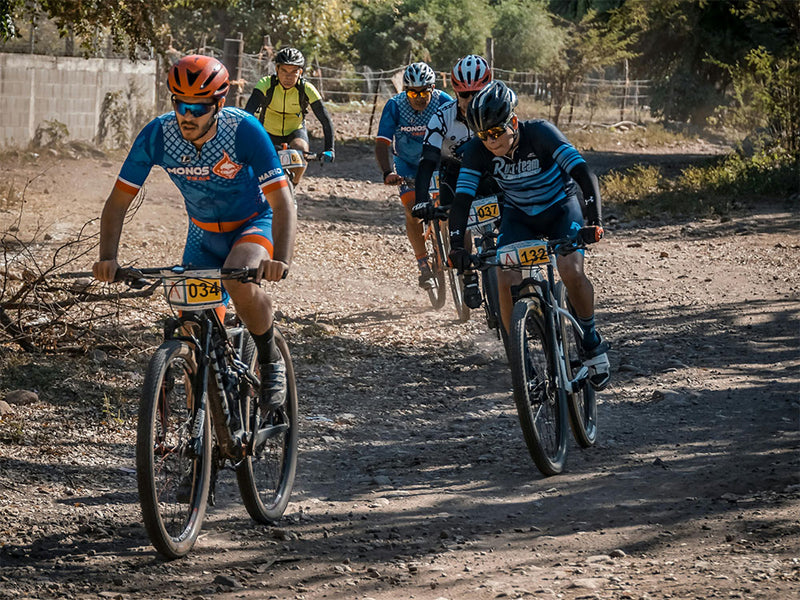 Bikers racing on a dirt track with trees and barriers in the background