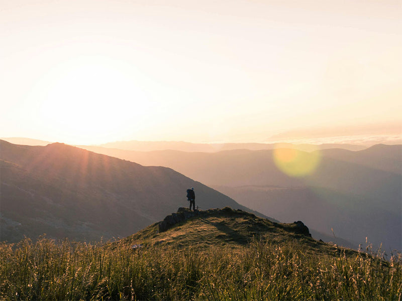 Person standing on a mountain peak with a sunset in the background